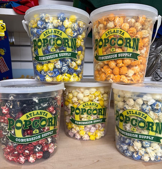 Five buckets of assorted popcorn from Atlanta Popcorn Concession Supply on a wooden surface.