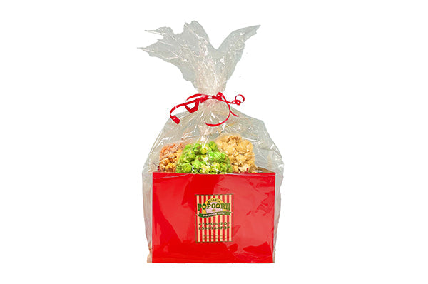 A red popcorn box filled with assorted popcorn and candy, wrapped in clear bag and tied with a red ribbon, on a white background.